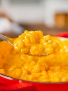 A spoonful of macaroni and cheese is raised from a pan, highlighting the rich, cheesy texture of this comforting dish.