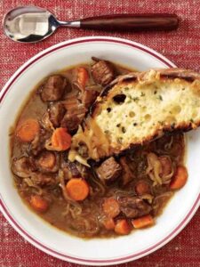 A bowl of hearty beef stew accompanied by a slice of bread, showcasing a comforting meal from Taste of Home Recipes.