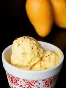 A bowl of the best ice cream topped with fresh mangoes, set against a vibrant mango backdrop.