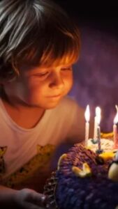 A young boy gazes at a purple birthday cake adorned with lit candles, embodying the joy of celebration and humor.