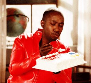 A man in a red jacket joyfully eats a cake, celebrating with a happy birthday theme.